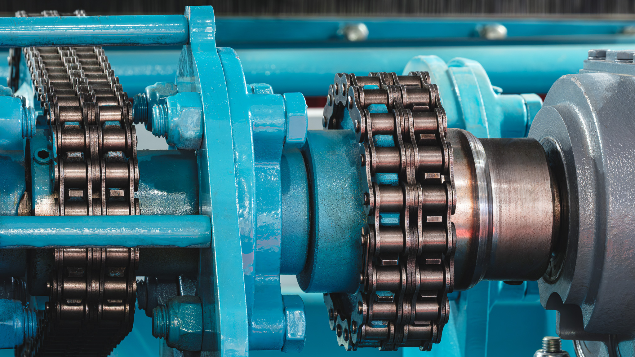 Blue machinery with silver metal gears and black roller chains showing mechanical drive system components