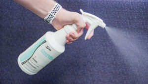 Hand holding white spray bottle of Kontrol Spray with green label against gray surface