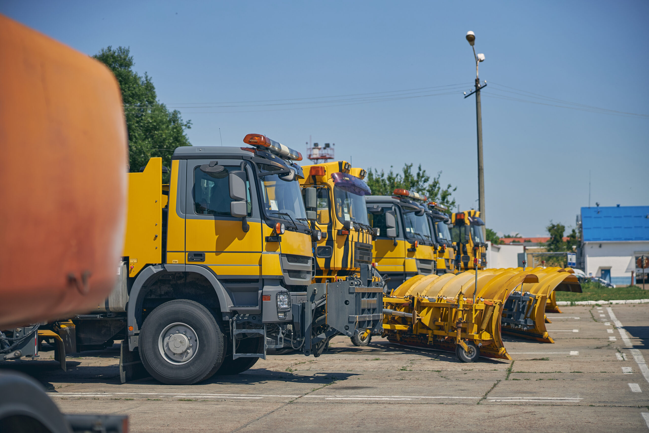Yellow and gray construction trucks parked on pavement under blue sky