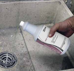 Person pouring white bottle with purple label into utility sink with drain
