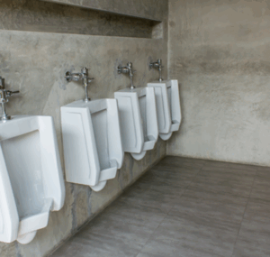Row of white wall-mounted urinals in commercial restroom with concrete walls and floors