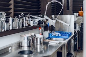 Commercial kitchen workspace with stainless steel prep table, sink, faucet, cookware and storage shelves