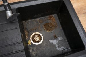 Dirty black commercial sink with clogged drain and built-up debris requiring professional cleaning service