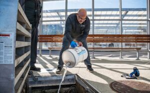 Technician pouring liquid lift station treatment chemical into a lift station