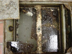 Corroded grease trap with heavy buildup and rust requiring chemical treatment or pump out