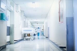 Clean, bright hospital corridor with white walls, medical equipment, and healthcare professionals in background