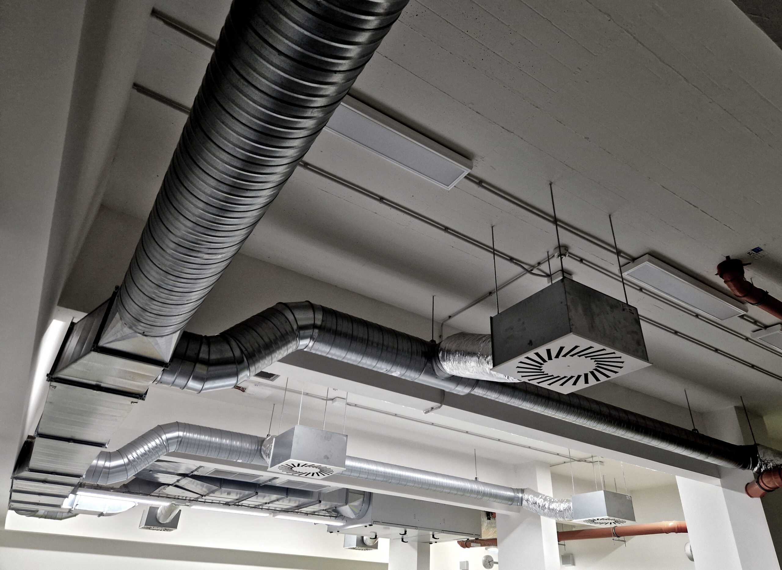 Commercial HVAC ductwork system with aluminum spiral ducts and ventilation units installed on ceiling