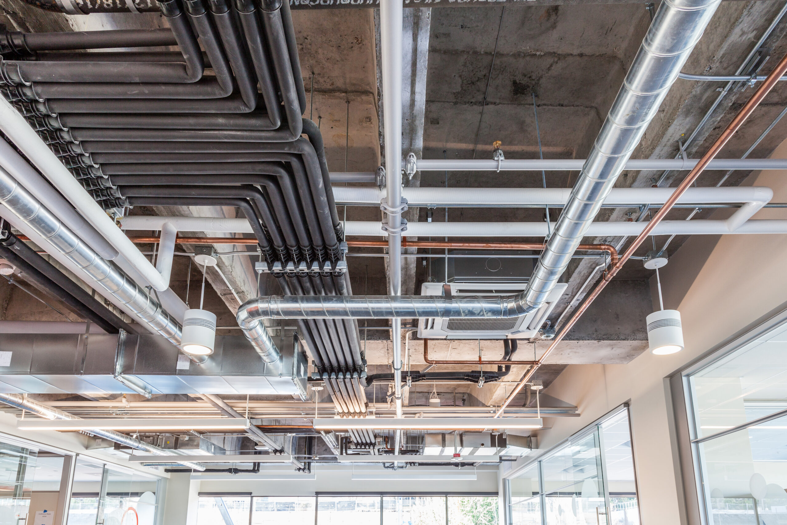 Exposed ceiling HVAC ductwork and piping system in commercial building mechanical space