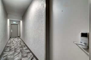 Modern hotel corridor with patterned carpet runner, white walls, and electronic door lock system