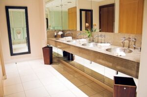 Modern commercial bathroom vanity with dual sinks, marble countertop, and wooden drawer storage