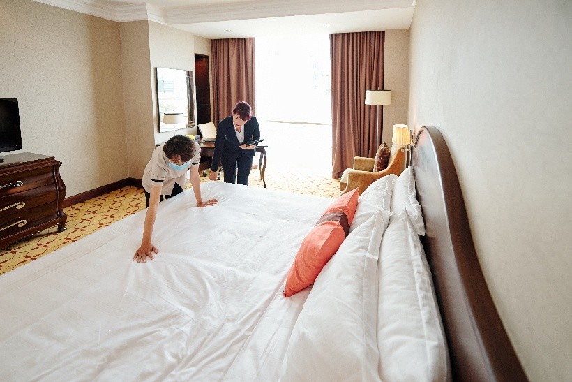 Family in hotel room with child playing while parents stand by window discussing accommodations