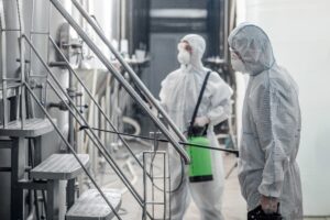 Two people in white protective suits and face coverings working with stainless steel equipment in a facility